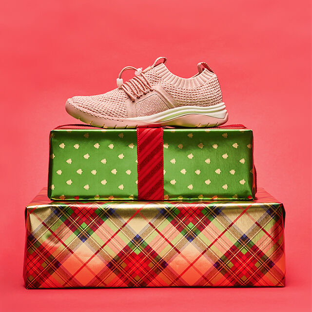Imagen de Torri en Dusty Rose, foto de perfil, encima de dos regalos de Navidad sobre un fondo rojo.